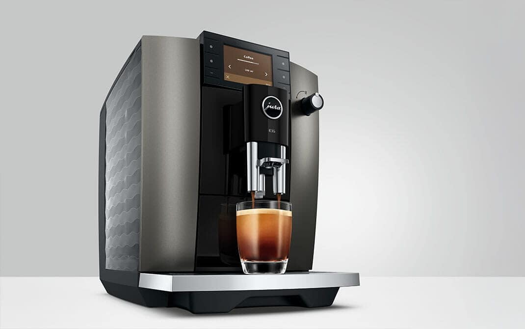 De nieuwe JURA E6 Dark Inox (ED) van opzij met verse koffie