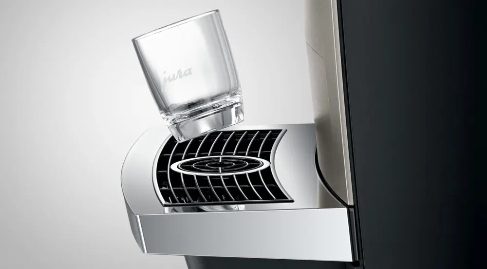 JURA X10c Dark Inox met een glazen kopje op het chromen lekrooster van de koffiemachine