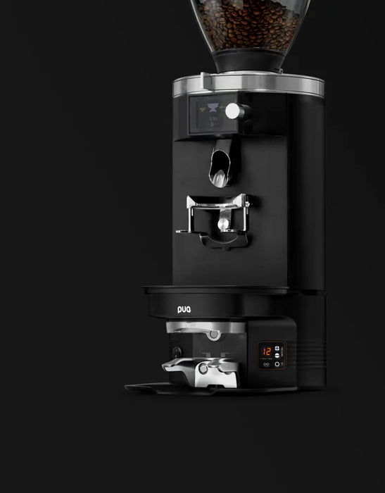 PuqPress M2 automatische koffiestamper onder een zwarte koffiemolen met digitale display en koffiebonenreservoir